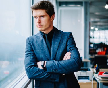 Zarif takım elbiseli beyaz erkek girişimci pencere kenarında duruyor iş fikri üzerine kafa yoruyor, resmi olarak giyinmiş, çapraz kollu müreffeh bir şirketin sahibi.