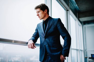 Resmi olarak giyinmiş düşünceli yakışıklı erkek yönetmen çatı katındaki pencereye bakarak gelecek planlarını düşünüyor. Zarif takım elbiseli, düşünceli, kendine güvenen beyaz iş adamı iş için fikirlere odaklanıyor.