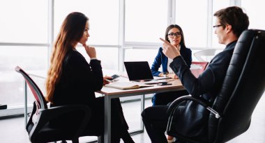 Profesyonel olarak giyinmiş erkek ve kadın iş arkadaşları planlama stratejisi için takım halinde çalışıyor, kadınlar mali müdürle görüşüyor ve ofiste birlikte oturup planlarını tartışıyorlar.