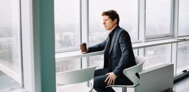 Resmi takım elbiseli, kendine güvenen bir erkek, elinde kahve bardağıyla fikirleri düşünürken başını çeviriyor. Kafkasyalı işadamı, iç işlerinde şirketlerin geleceğini düşünüyor.