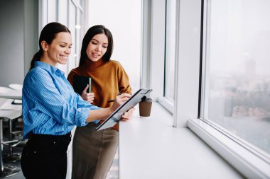 Neşeli kadın çalışanlar başarılı proje planlama raporlarından memnunlar. Tatilde birlikte rapor okuyorlar. Kafkasyalı mutlu kadınlar kağıtları kontrol ediyor ve içişlerinde kahveyle duruyorlar.