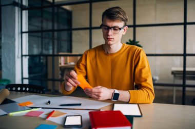 Gözlüklü düşünceli hippi adam elinde renkli çıkartmalar tutuyordu ve onu çizim için kullanıyordu. Konsantre olmuş erkek mimar elinde kağıt planlarla masaüstünde oturuyordu.