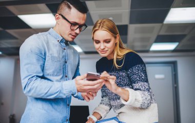 Gündelik giyinmiş iki genç adam ve kadın ofiste duran modern akıllı telefon cihazının internet sitesinde yazı yazıyorlar. Hücresel ağlarda video izleyen hippi öğrenciler