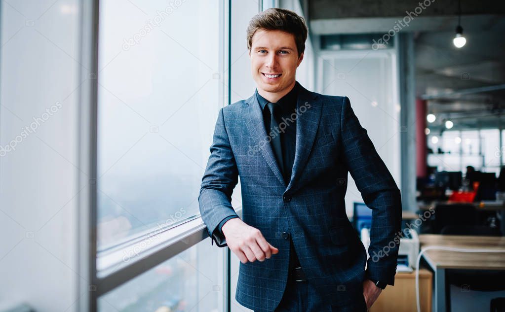 Half length portrait of prosperous caucasian male owner of corporation dressed in elegant suit standing in office, prosperous businessman in formal wear looking at camera satisfied with success in job