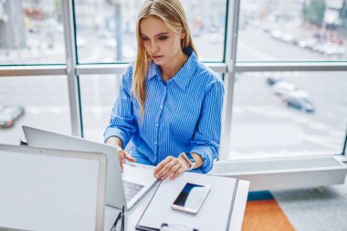 Modern dizüstü bilgisayarda yayınlamak için kablosuz internet kullanan düşünceli genç bir kadın. Ofisteki masaüstünde oturan netbook 'ta kadın grafik tasarımcısı bilgi arıyor.