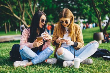 Hippi kızlar, modern cep telefonlarına yeni bir uygulama yüklemek için boş vakitlerini kahve ile parkta geçiriyorlar. Kadın arkadaşlar, bluetooth bağlantısıyla dışarıda dinlenirken multimedya dosyalarını paylaşıyorlar.