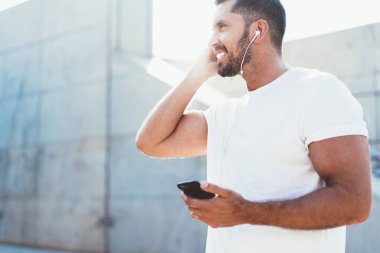 Boş tişörtlü, mutlu ve mutlu bir adamın bakışları. Motivasyon konsepti olan sesli kitapları dinlerken gülümsemesi. Elektronik kulaklıklı neşeli bir erkek.