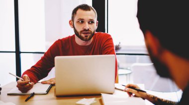 Ciddi bir beyaz erkek yönetici, iş yerinde dizüstü bilgisayarla oturup çalışanlarla görüşüyor. Kendine güvenen otobüs sahibiyle yapılan röportajın görüntüsü.