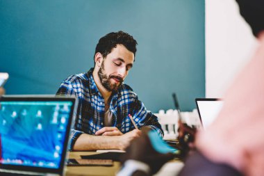 Günlük giyimde çalışan çalışanlar ofiste oturan yazı planı ve fikirler üzerinde yoğunlaşmışlar. Kafkasyalı yaratıcı tasarımcı projec fikirleri üzerine kalemle kafa yorarak skeç çiziyor.