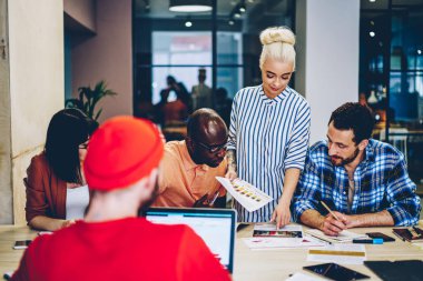 Genç profesyonel bayan antrenör, öğrencilerden oluşan bir ekibe eğitim atölyesi dersi veriyor. Grafikler ve planlar üzerinden bilgi açıklıyorlar. Çok ırklı çalışanlardan oluşan bir ekip mali temsilciyi kontrol ediyor.