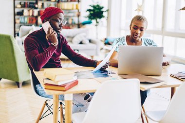 Koyu tenli bir adam, cep telefonuyla kadın meslektaşıyla çalıştığını bildiriyor. Erkek, servis operatörünü telefonla ararken kız arkadaşının yanında oturuyor.