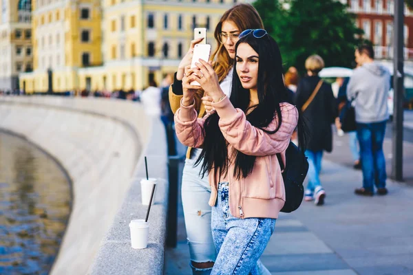Çekici esmer ve sarışın kadın turistler şehir ortamının resimlerini çekmek için cep telefonu kullanıyor, cep telefonu blogcuları ellerinde cep telefonlarıyla ağlardaki takipçilerle paylaşmak için fotoğraf çekiyor.