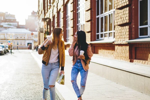 Happy caucasian girls best friend having fun during conversation with coffee to go walking in downtown in spring, happy tourists laughing during sightseeing tour resting together on vacations