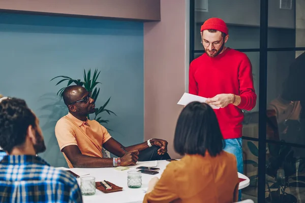 Serious team leader reading information report during meeting with company colleagues , multiracial male and female group listening to coach checking financial planning for business startup in offic