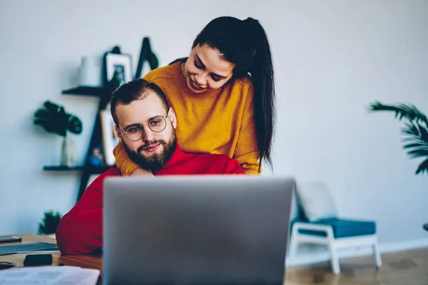 Vrolijke Jonge Vrouw Knuffelen Haar Vriend Terwijl Hij Werkt Freelance — Stockfoto