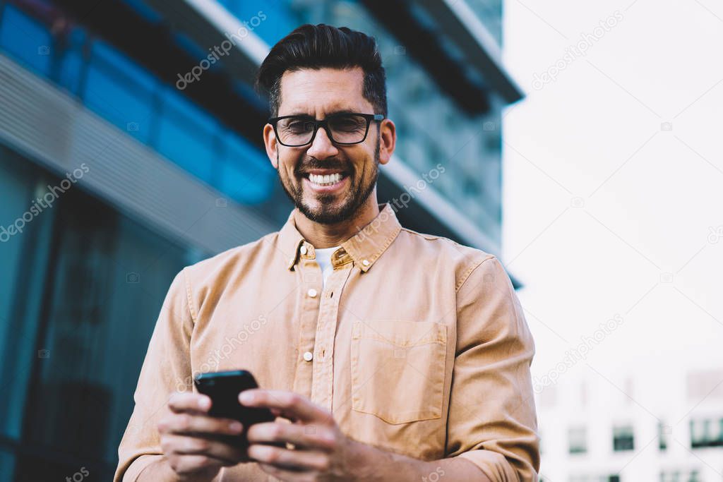 Half length portrait of happy emotional man in spectacles for vision correction looking at camera and laughing during time for using modern technology, concept of communication and digitalisation