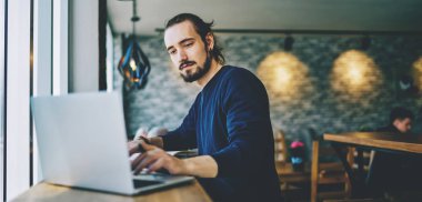 Kafkasyalı öğrenci dizüstü bilgisayarda webinar izliyor programlama becerilerini geliştiriyor, ciddi profesyonel web tasarımcısı kafeteryada serbest çalışıyor ve iyi bir wifi bağlantısı kullanıyor.
