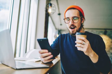 Şaşırmış hipster adam cep telefonundan şok edici içerik haberleri izliyor ve merak ediyor. Şaşırmış erkek blogcu bir mesaj aldı. Millennial 'dan bir adam, alışveriş promosyonları için arıyor.