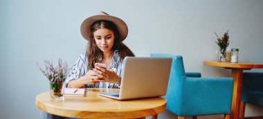 Genç Kafkas kadın blogcu, sosyal ağlarda cep telefonuyla kapalı mekanlarda multimedya dosyalarını paylaşıyor, Wi-Fi 'ye internet bağlantısı olan genç bir kadın başvuru masasında oturan arkadaşlarıyla sohbet ediyor.