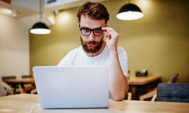 Görme koruması için gözlüklü konsantre hipster adam birlikte çalışma alanında dizüstü bilgisayarla çalışıyor. Netbook 'taki derslerden ders alan zeki erkek öğrenci.
