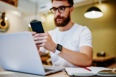 Erkek akıllı telefon üzerine seçici odaklanma. Multimedya dosyalarını dizüstü bilgisayarla senkronize eden geliştirici. Modern aletleri kullanan genç hippi adam ve internetteki çalışma alanı için internet bağlantısı.