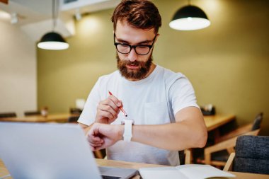 Akıllı ekranda ayarlar yaparken dizüstü bilgisayarda çalışan yetenekli erkek serbest yazar. Konsantre hipster adam, çağdaş kol saatinde Wi-Fi kullanarak GPS 'i takip ediyor.