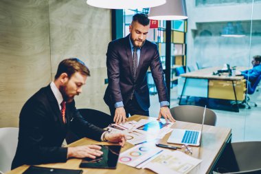 Takım elbiseli başarılı bir CEO iş planını açıklıyor ve modern dokunmatik pedi iş için kullanan yaratıcı erkek çalışanlara iş veriyor. Ofisteki tüccarla iletişim kuran finans şirketinin sahibi.