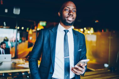 Başarılı bir Afrikalı Amerikalı girişimci takım elbiseli, gülümseyen ve dik bakan. Başarılı bir erkek CEO 'yum. Modern ofis içinde elimde akıllı telefonlar, planlar ve hayaller kuruyorum.