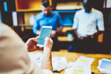 Açık kopya alanı olan akıllı telefondaki uygulamada yazıya erkek eli yazmaya odaklan. Ofisteki meslektaşları arka planda dururken cep telefonu kullanan cep telefonu ve iş adamının kırpılmış görüntüsü