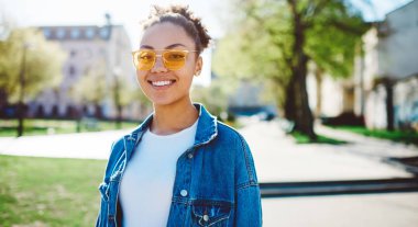 Neşeli Afrikalı bir genç kızın yakın portresi. Hafta sonu güneşli bir bahar günü, kot ceketli mutlu bir hippi kız. Gülümsüyor ve kameraya bakıyor.