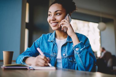 Mutlu siyahi kız öğrenci otokopi için eğleniyor ve sınava hazırlanırken akıllı telefon uygulamasını kullanarak arkadaşını arıyor, başarılı hipster kız cep telefonuyla konuşuyor.
