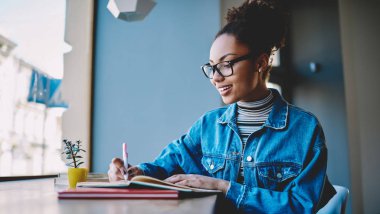Neşeli kadın blogcu, içerik için ilginç bir fikir yaratmaktan heyecan duyuyor, bir sonraki yayınına kadar, mutlu koyu tenli öğrenci okul sınavı için bilgi hazırlamak için kafeteryada zaman geçiriyor.