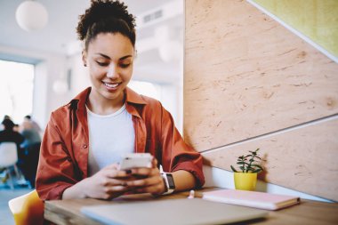 Afro-Amerikalı kadın blogcu mobil iletişim uygulaması üzerinden sohbetten zevk alıyor, pozitif hipster kız cep telefonuyla internete baktığı için komik metinlerle posta yazıyor.