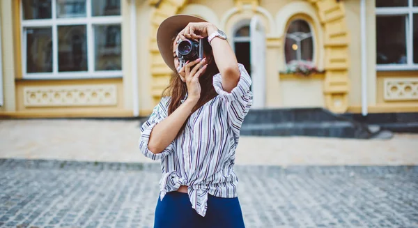 都会の中に立つレトロなカメラで写真を撮る熟練した女性写真家 流行の帽子をかぶった白人女性 街を旅するアパレル写真を撮る趣味を楽しむ — ストック写真