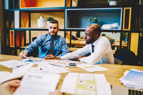 Two diverse executive managers dressed in shirts collaborating on development business plan of financial company. Proud ceo talking with professional trader about entrepreneurship and innovation