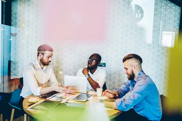 Experienced multicultural entrepreneurs in formal wear communicating with each other and discussing plan of collaboration on common project during meeting. Partnership of professionals in office