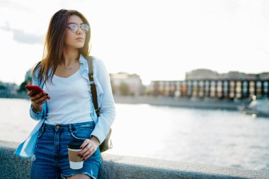 Sıradan giyinmiş çekici genç bir turist elinde kahveyle içeri giriyor ve akıllı telefondaki profilini güncelliyor. Gezide başka bir yere bakıyor ve güzel şehrin manzarasının tadını çıkarıyor.