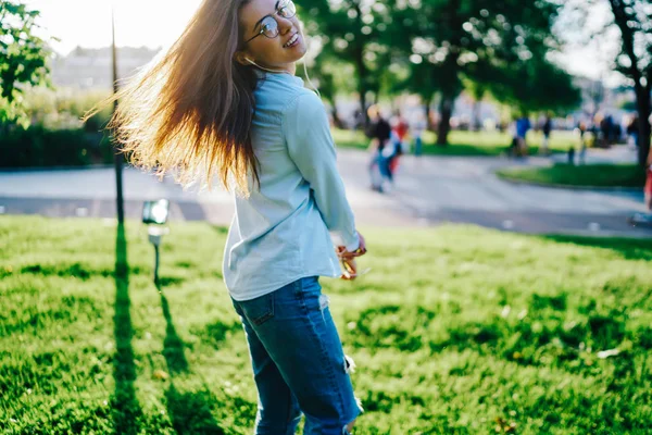 美しい髪の毛を持つ魅力的な陽気な若い女性は イヤホンでオーディオを聞いて 晴れた週末を楽しんで緑の公園で踊ります — ストック写真