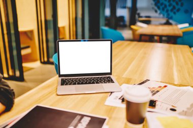 Bilgisayarında maket ekran var. Çalışma yerinde duruyor. Yanında eşyalar ve kahve fincanı var. Kablosuz internete bağlı açık bir defter.