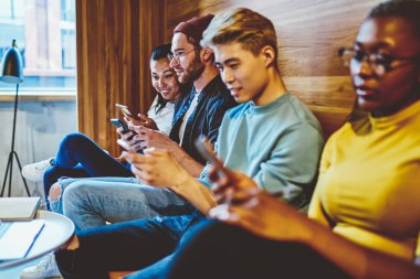 Çağdaş teknoloji düşkünü genç nesil hipsterler online sohbet ve ağ kurma bağımlısı, pozitif çok ırklı erkek ve kadınlar akıllı telefonlarla birlikte oturuyorlar iletişimi görmezden geliyorlar.