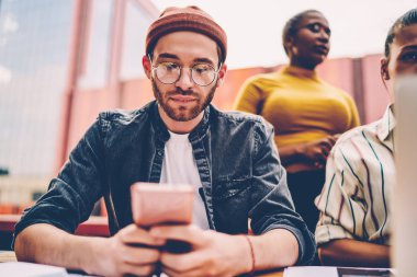 Havalı hippi adam akıllı telefondan mesajlar alıyor ve sosyal ağlarda sohbet ediyor birlikte çalışma alanındaki 4G internet bağlantısını kullanıyor. Cep telefonuyla günlük giyinmiş genç adam blogu yazıyor.