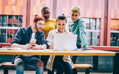 Gelişigüzel giyinmiş pozitif çok kültürlü arkadaşlar dizüstü bilgisayarda oturup internet sitesinde komik dersler izliyorlar. İnternetteki kablosuz interneti kullanarak. Neşeli gençler netbook 'a uygulama yüklüyorlar.