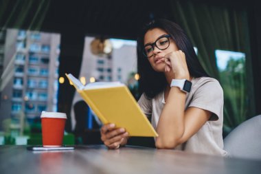Görme düzeltmesi için gözlüklü dalgın hippi kız kafeteryada boş zaman üzerine ilginç bir kitap okumaya odaklan. Kafkasyalı genç bir kadın edebiyat romanıyla boş zamanlarını kafede geçiriyor.
