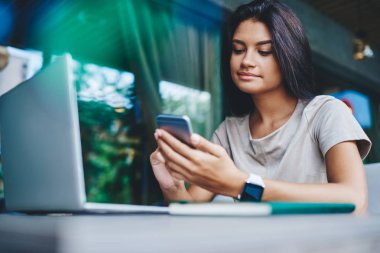 Sosyal ağlarda yeni beslemeleri kontrol eden genç hippi kız boş zamanlarında kafede netbook 'la oturuyor, olumlu milenyum kadını internetteki uzak iş için kablosuz bağlantıyı kullanarak multimedya dosyalarını paylaşıyor