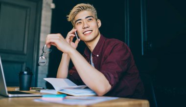 Hayalperest Çinli genç adam elinde gözlük tutuyor ve arkadaşlarıyla birlikte akıllı telefondan arıyor. Telefondan konuşan Japon hipster blogcu iş birlikçi dizüstü bilgisayarın başında oturmuş gülerken...