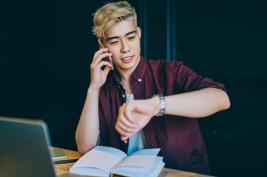 Şık sarışın hippi öğrenci akıllı telefondan ararken saati kontrol ediyor ve arkadaşlarıyla konuşuyor. Genç adam cep telefonuyla iletişim kurarken kol saati yönetiyor.