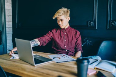 Modern uzayda kablosuz internet kullanarak modern dizüstü bilgisayarda webinar çalışmasını izleyen düşünceli Çinli hippi öğrenci. Netbook Cihazı 'nda serbest çalışan Milenyum Asyalı genç adam.