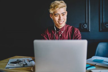 Sıradan giyinmiş neşeli Çinli hippi internet sitesinde internet bağlantısı kullanarak dizüstü bilgisayara bağlı dijital kulaklıklarla müzik dinliyor. Modern uzayda masaüstünde otururken