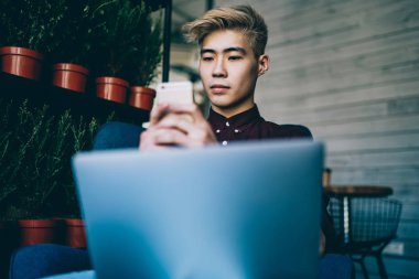 İletişim için akıllı telefonlarda yüksek hızlı internet bağlantısını kullanan yeni nesil milenyum. Çinli hipster blogcu cep telefonuyla sohbet ediyor. Laptop bilgisayarında birlikte çalışıyor.