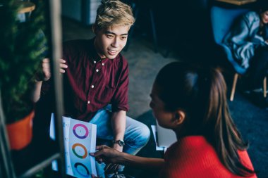 Asyalı yakışıklı hippi adam, Çin 'li genç bir kadını elinde tutan ve modern uzayda dikkatlice dinleyen bir meslektaşı olan kağıt resimle finansal verileri diyagramda açıklıyor.